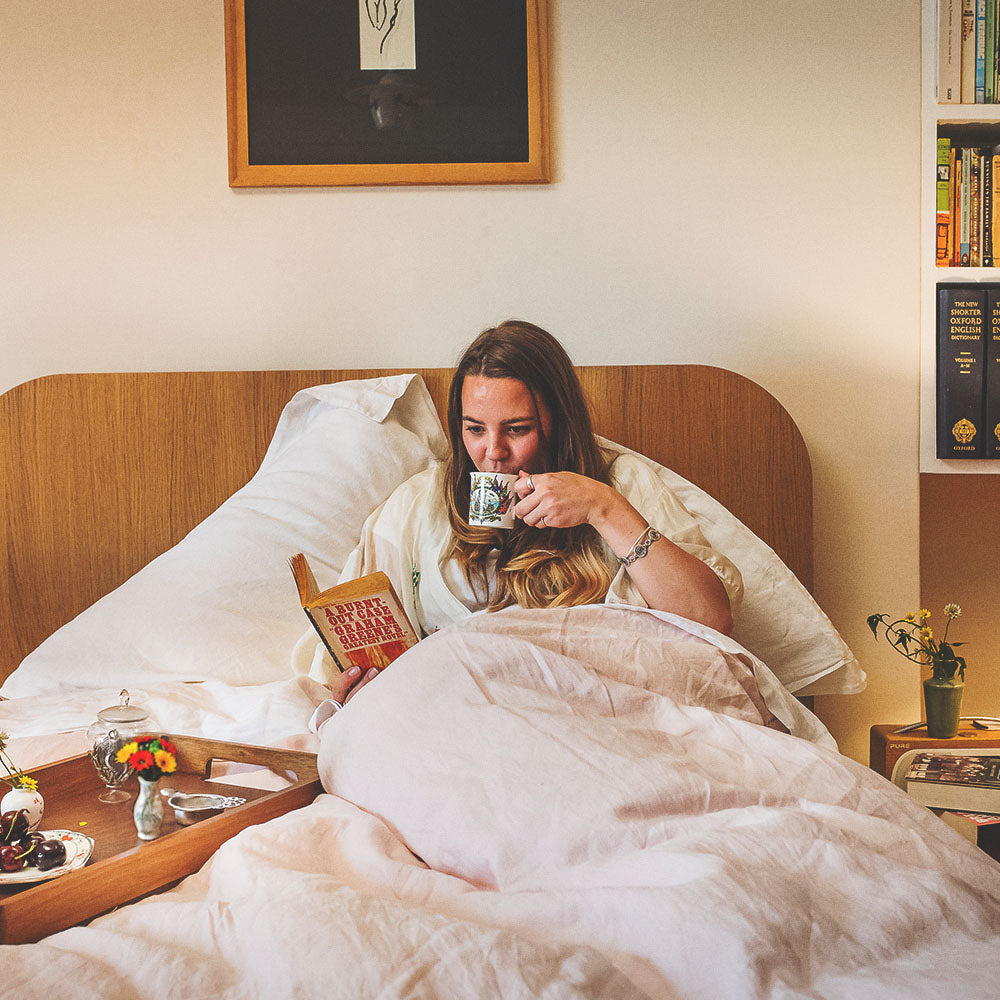 women enjoying a cup of chamomile tea in bed reading a book