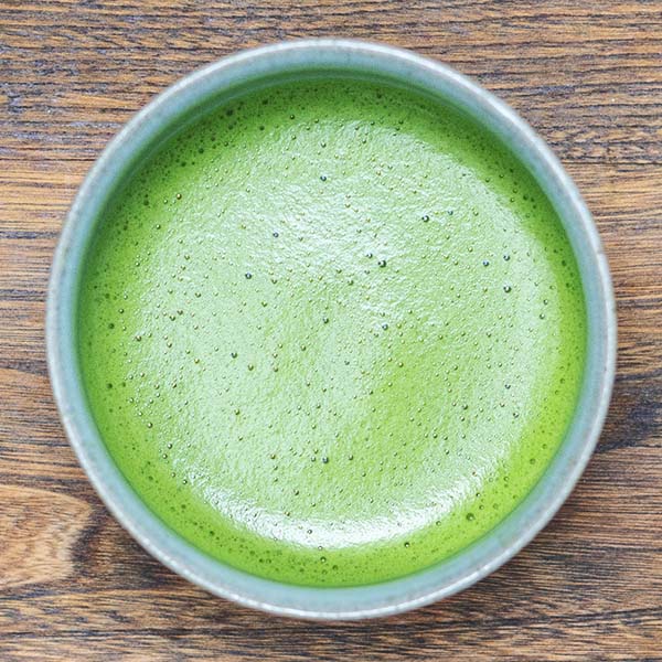 A traditionally whisked ceremonial matcha in a matcha bowl on a wooden surface.