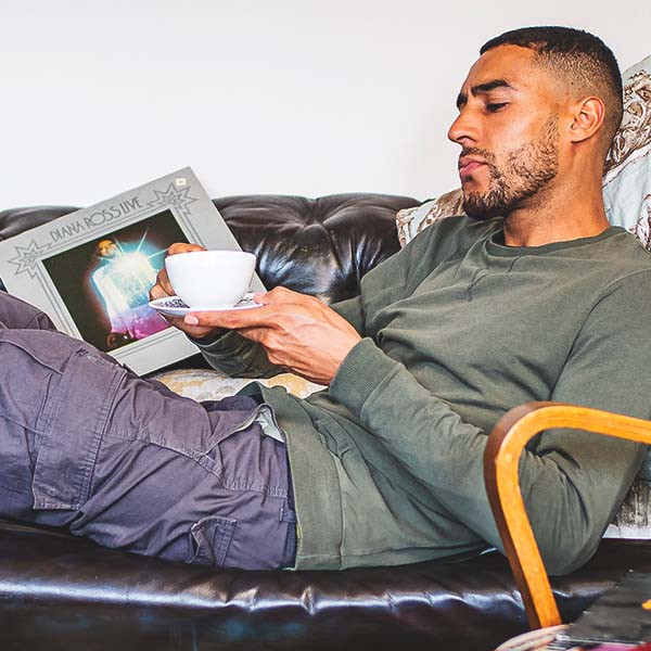 Man lounging on a couch holding a tea cup, with a casual and relaxed atmosphere.