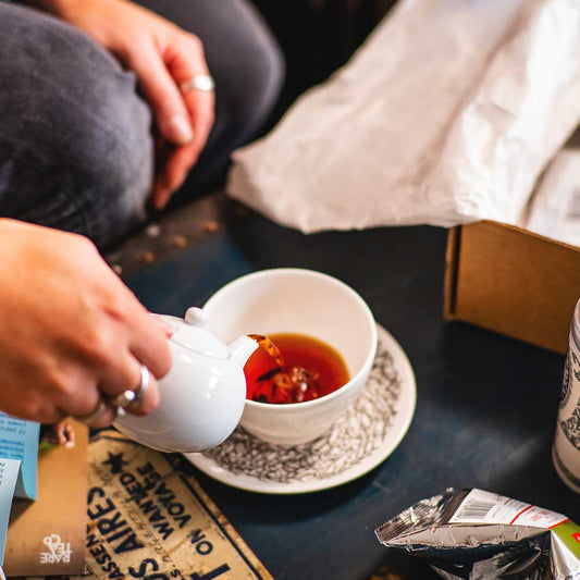 Person pouring tea from a teapot into a tea cup, with a tin of Rare Tea Company Rare Earl Grey and an opened delivery box in the background.