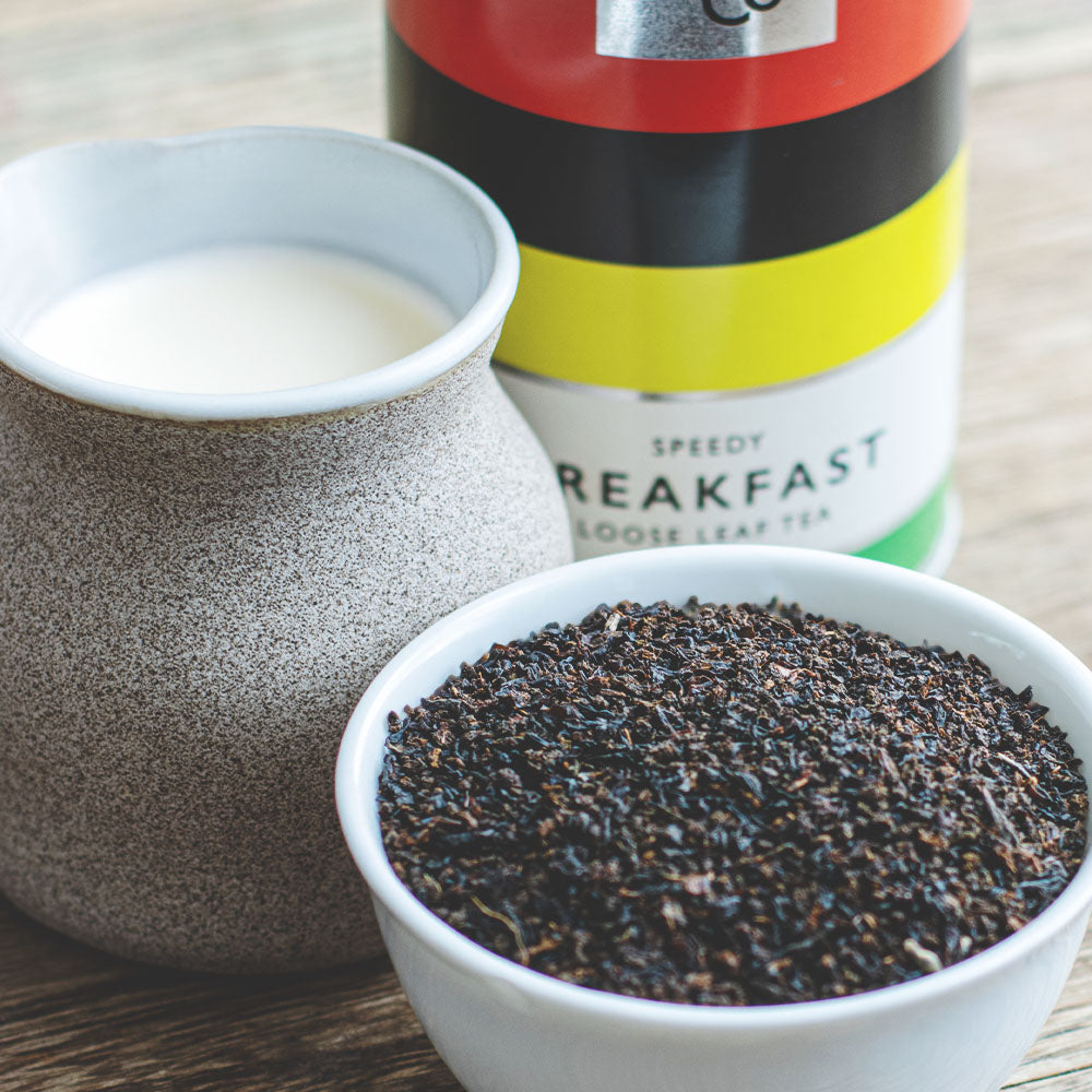 bowl of loose leaf english breakfast tea next to a jug of milk and a tin