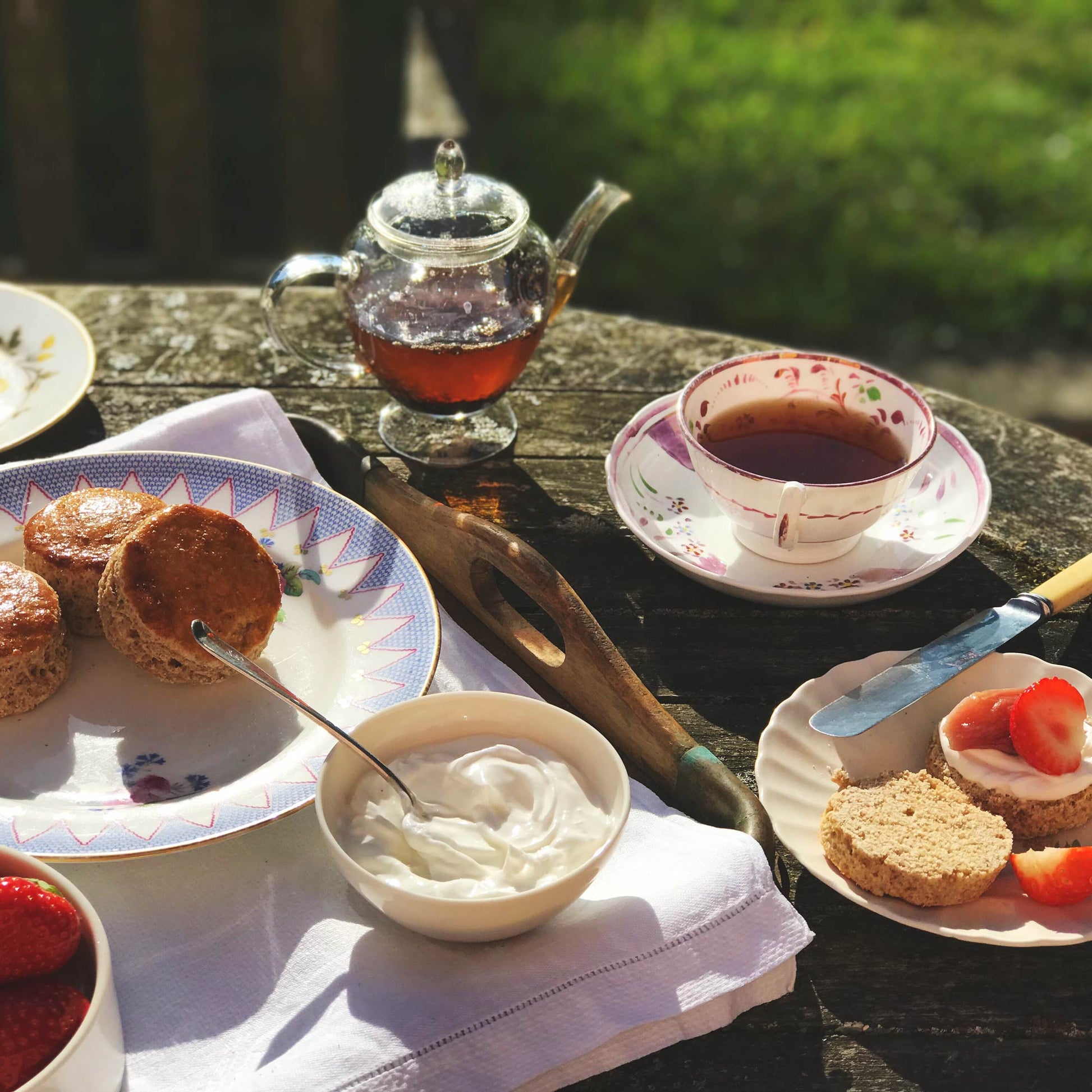 a picnic bench of afternoon tea alongside a cup of our Rare Afternoon Tea in a mug